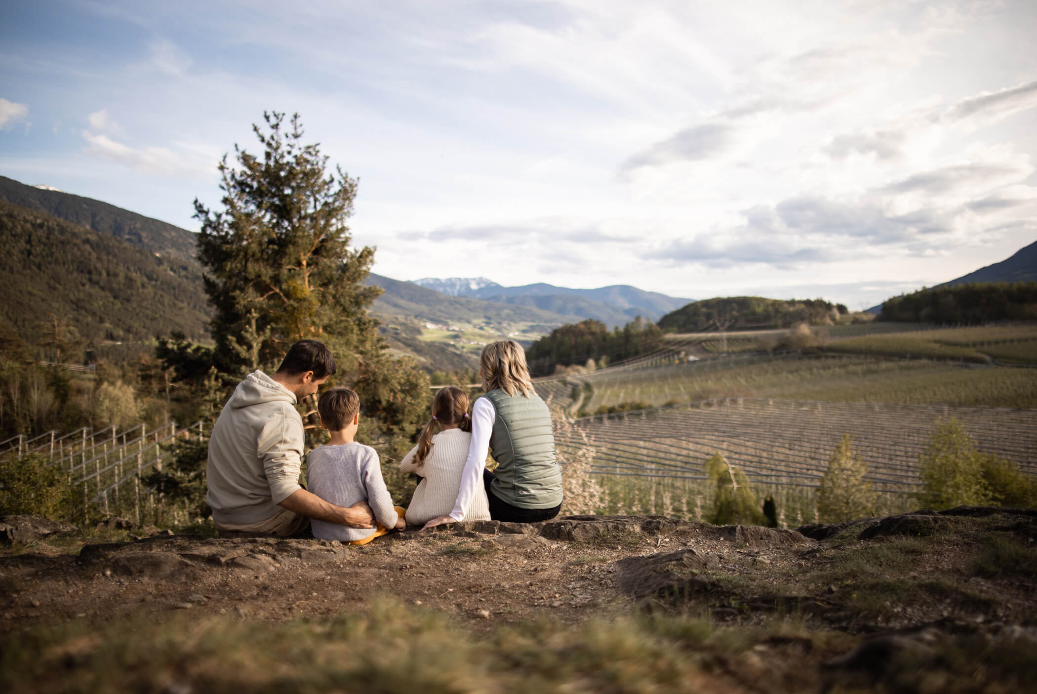 A family sits on stones and looks out over the apple orchards - Schirmerhof