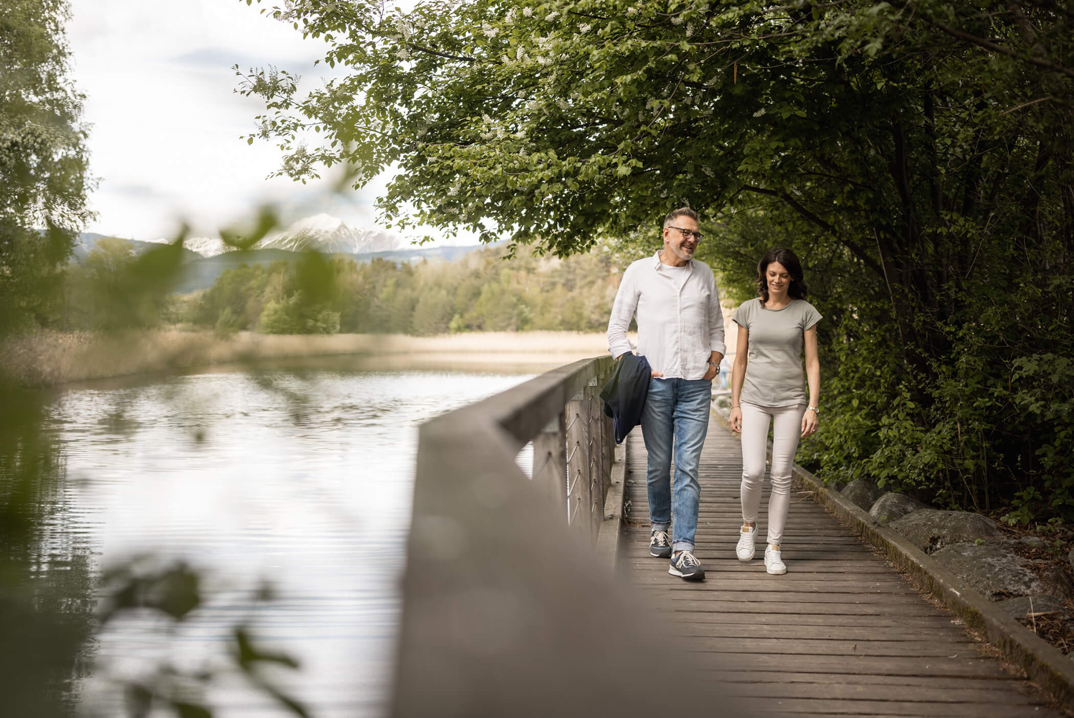 A couple walks across a bridge, next to a lake - Schirmerhof